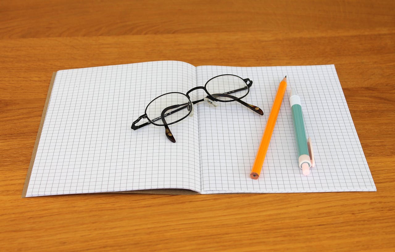 Open notebook with graph paper, eyeglasses, and pencils on a wooden table.