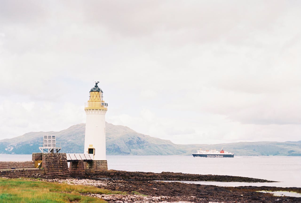 Scenic view of a lighthouse on Isle of Mull with a ship sailing on the calm sea.